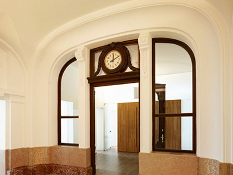 Elegantes Innenraum-Foyer mit klassischen weißen Bögen, Holztüren und antiker Uhr über dem Durchgang
