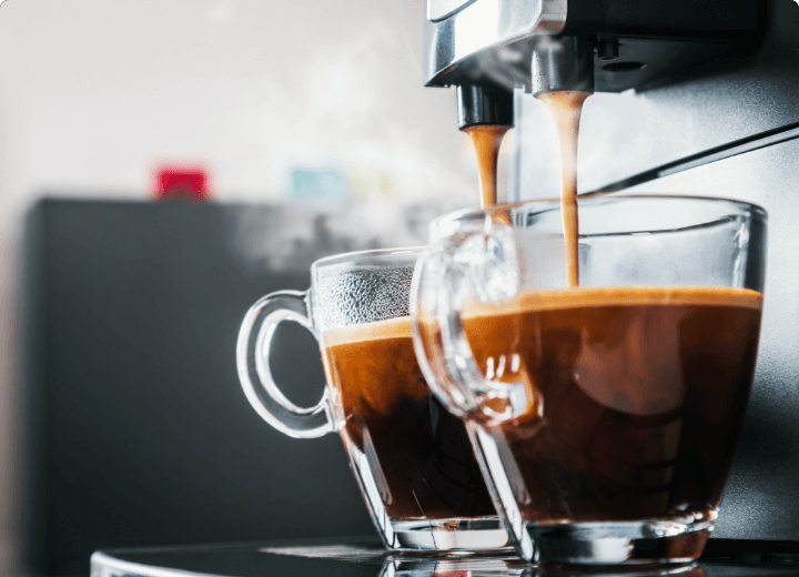 Frisch gebrühter Kaffee läuft aus einem Kaffeevollautomaten in zwei Glastassen mit Crema