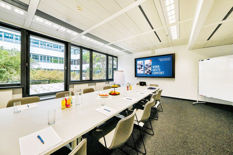 Heller, geräumiger Konferenzraum mit großem Besprechungstisch, Präsentationsbildschirm mit Aufschrift 'Work Meets Comfort' und Blick auf den Innenhof im EuroPlaza.