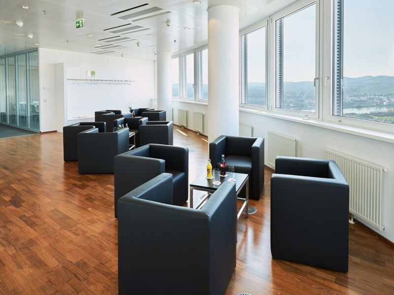 Moderne Büro-Lounge mit schwarzen Ledersesseln, Parkettboden und großen Fenstern mit Blick auf eine malerische Landschaft
