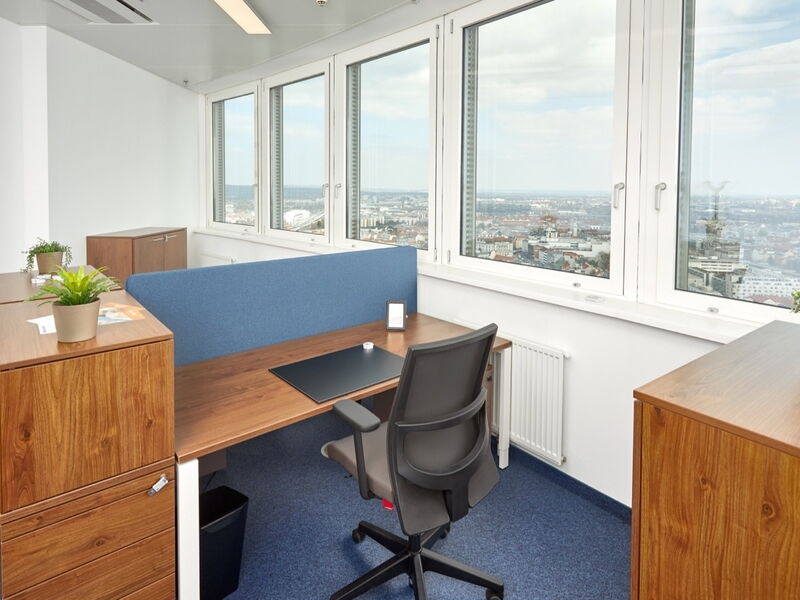 Modernes Büroarbeitszimmer mit einem Holztisch, ergonomischem Bürostuhl, blauer Trennwand und großen Fenstern mit Blick auf die Stadt.