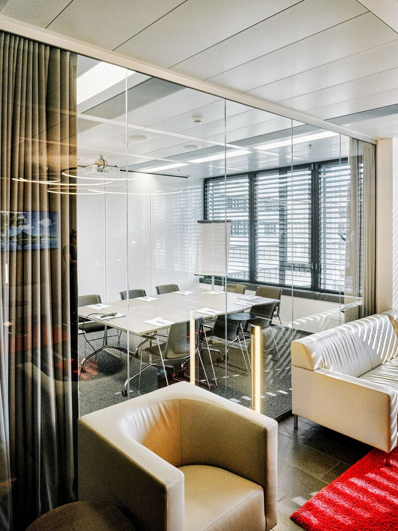 Modernes Bürointerieur mit einem gläsernen Konferenzraum, großem Holztisch und ergonomischen Stühlen