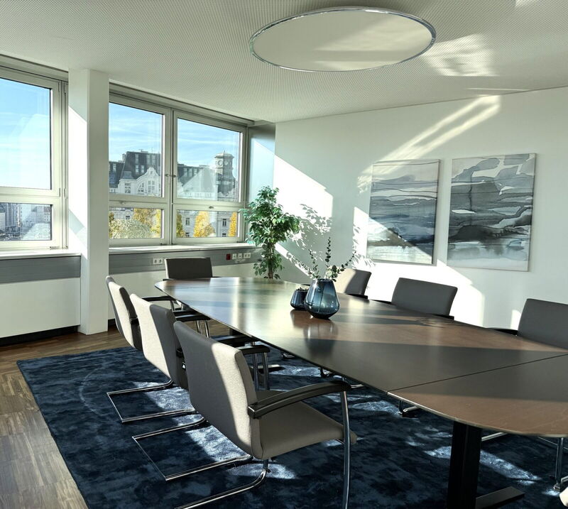Geräumiger Konferenzraum mit großem Holztisch, bequemen grauen Stühlen und großen Fenstern mit Stadtblick im YOUR OFFICE Akademiehof.