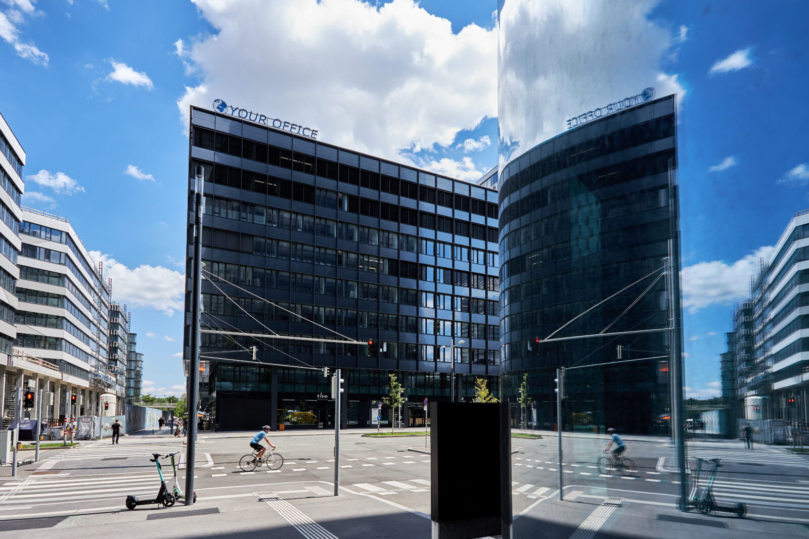 Modernes dunkles Bürogebäude mit Your Office Logo in einer Straßenszene mit Radfahrer und Spiegelung