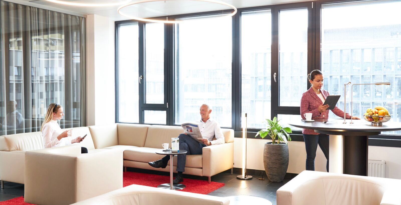 Employees working and relaxing in a bright modern office lounge area with large windows