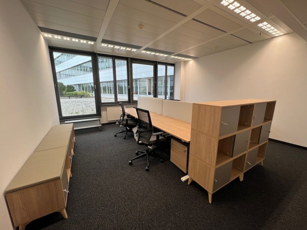 Heller, moderner Büroraum mit Holztischen, ergonomischen Bürostühlen und modularen Regalen.