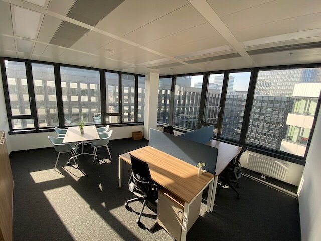 Bright and modern open-plan office space with desks, ergonomic chairs, and large panoramic windows offering a city view