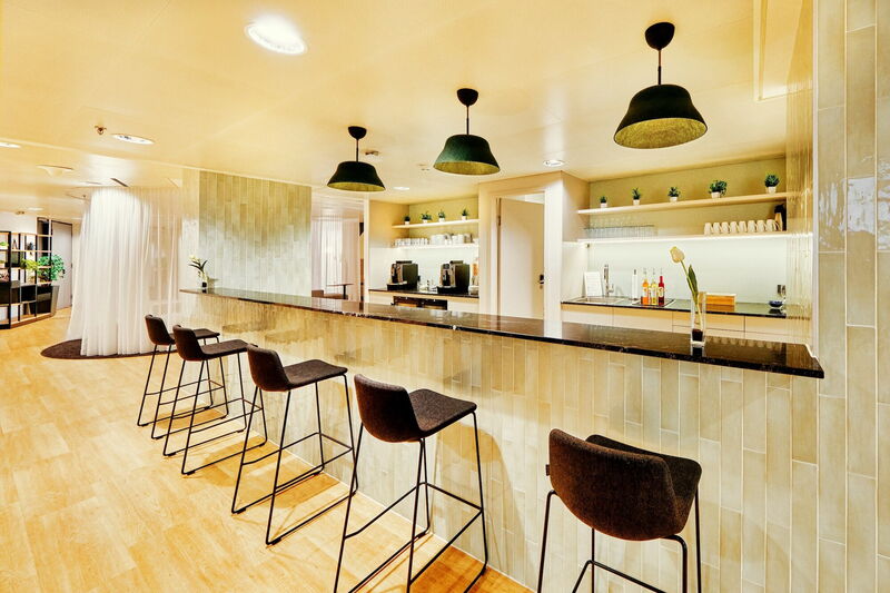 Moderne Office-Teeküche mit langer gefliester Bar, hohen Barhockern und stilvollen Hängeleuchten im EuroPlaza.