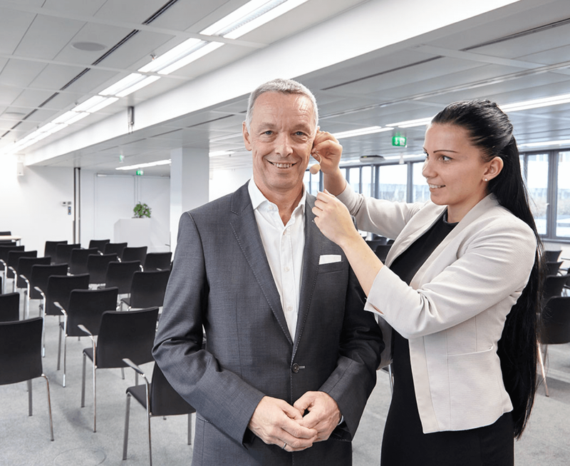 A woman helping a businessman adjust his headset microphone before a conference event in a modern meeting room