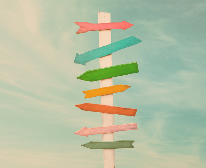A vintage wooden signpost with multiple colorful pointing arrows against a cloudy sky