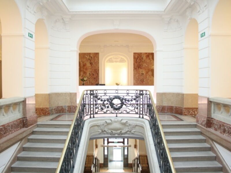 Elegantes Treppenhaus mit kunstvollem Eisengeländer in einer hellen historischen Eingangshalle mit Marmor-Akzenten