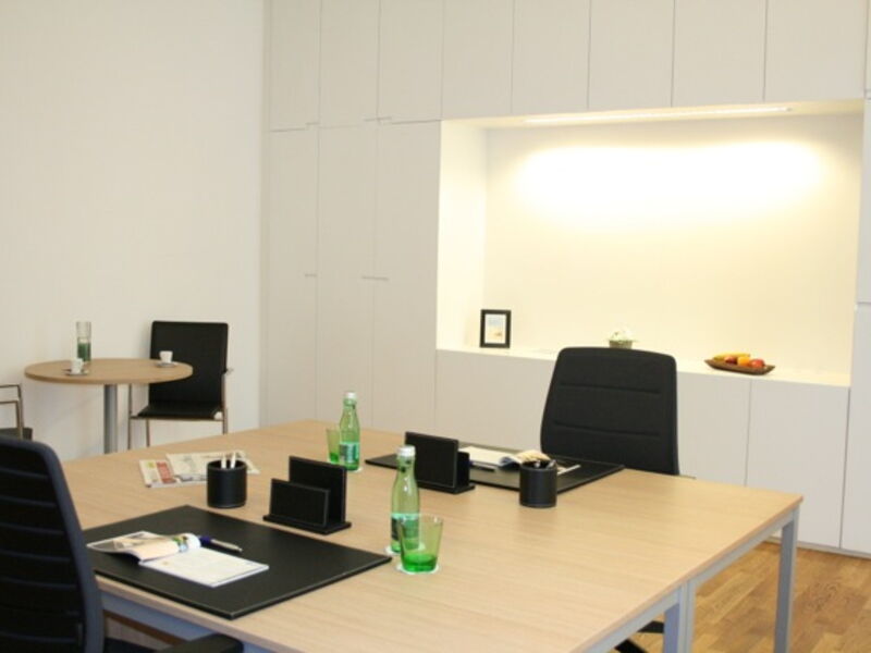 Moderne Büroinneneinrichtung mit großem Holztisch, weißen Oberschränken und indirekter Beleuchtung.