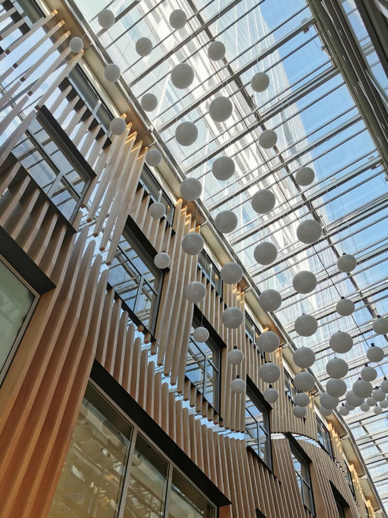 Blick nach oben in ein modernes mehrstöckiges Gebäude mit Glasdach und zahlreichen hängenden kugelförmigen Lampen