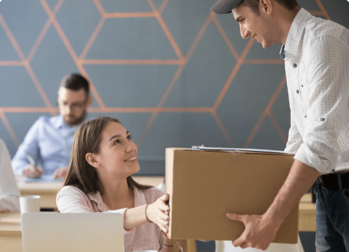 Ein freundlicher Zusteller liefert ein Paket an eine lächelnde Mitarbeiterin im Büro