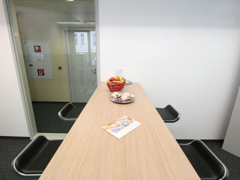 Moderner Pausenraum im Büro mit einem langen Stehtisch aus Holz, schwarzen Barhockern, einer Obstschale und einer Glastrennwand im Euro Plaza