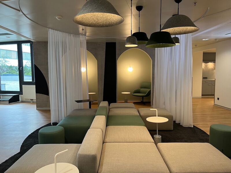 Modernes Büro mit modularen grau-grünen Sofas, Akustik-Filz Pendelleuchten und gemütlichen Nischen mit Vorhängen.