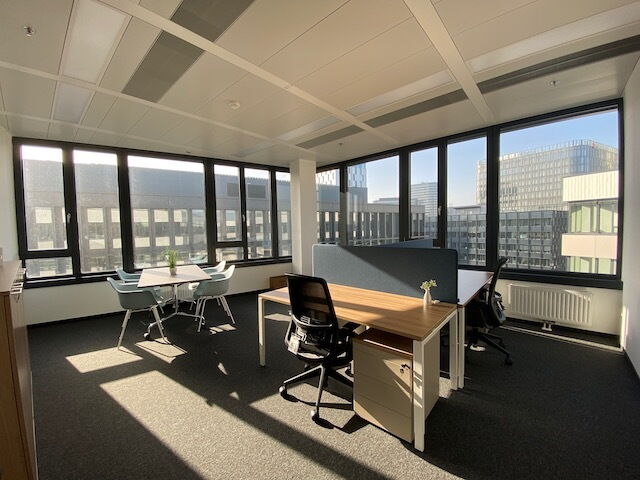 Heller, moderner Büroraum mit Holztischen, ergonomischen Stühlen und großen Fenstern mit Blick auf die Stadt
