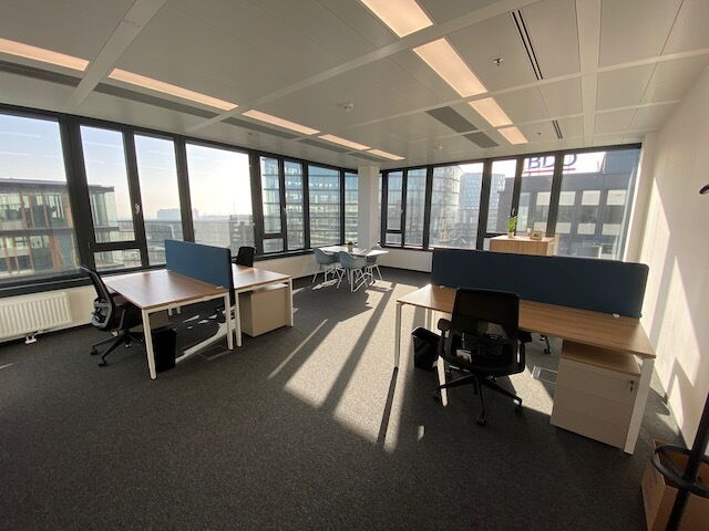 Heller und moderner Großraumbürobereich mit Holztischen, ergonomischen Stühlen und großen Panoramafenstern mit Blick auf die Stadt.