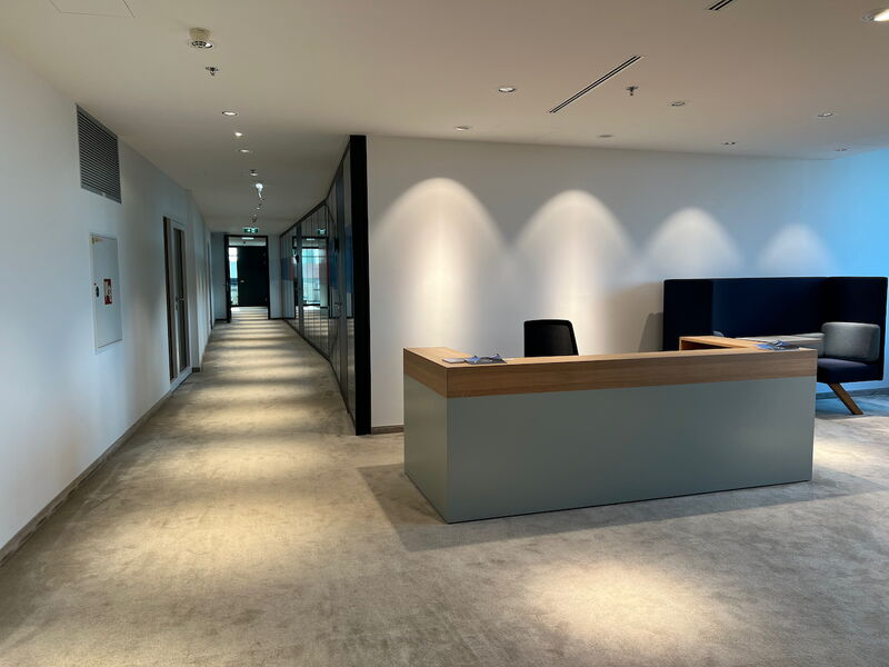 Moderner Empfangstresen in einem hellen Flur mit Teppichboden und Glasabtrennungen im Bürogebäude
