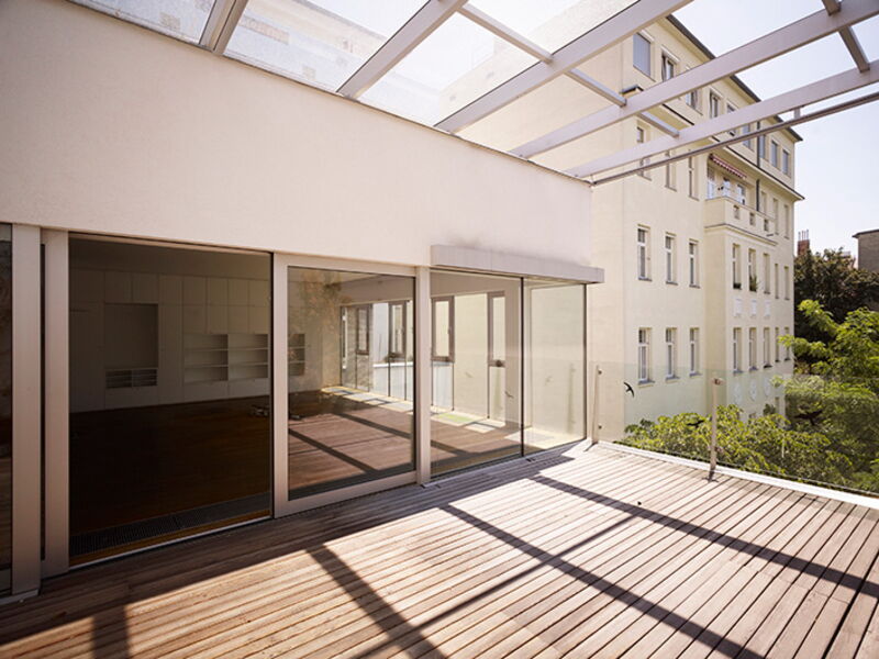 Geräumige moderne Galerieterrasse mit Holz-Dielen, großen Schiebetüren aus Glas und Glasdach mit Blick auf historische Architektur