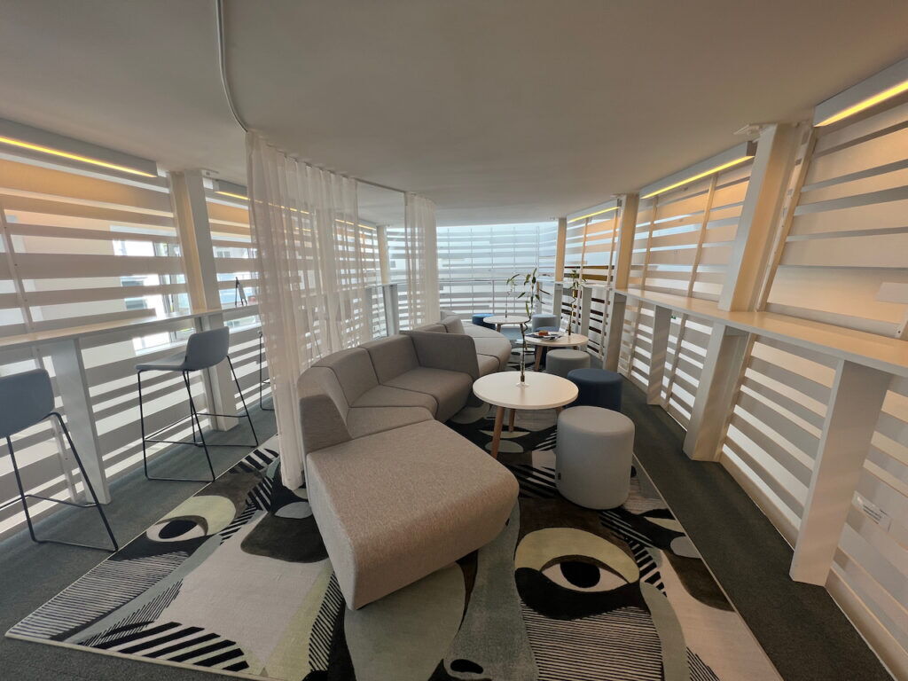 Bright and modern breakout area in an office with comfortable seating, a unique artistic rug, and wooden slatted wall partitions.
