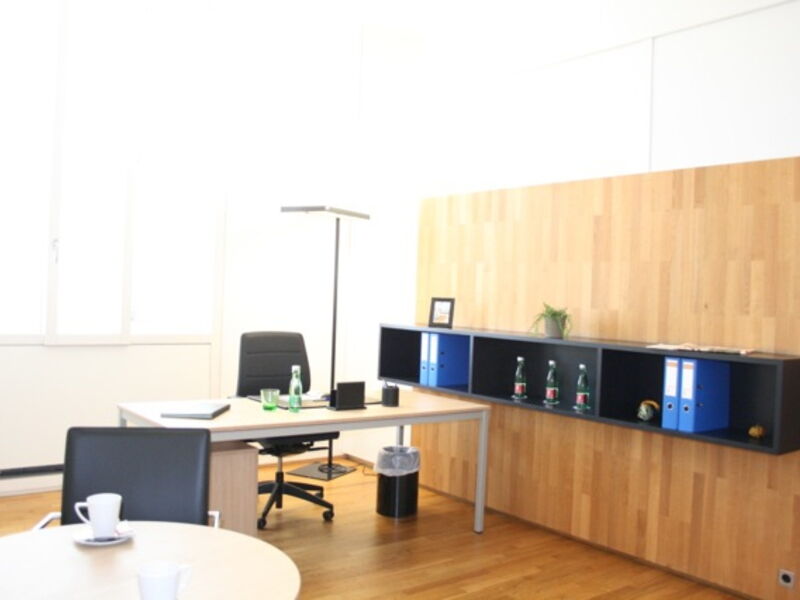 Helles, modernes Büro mit Holzschränken, ergonomischen schwarzen Bürostühlen und aufgeräumten Schreibtischen.