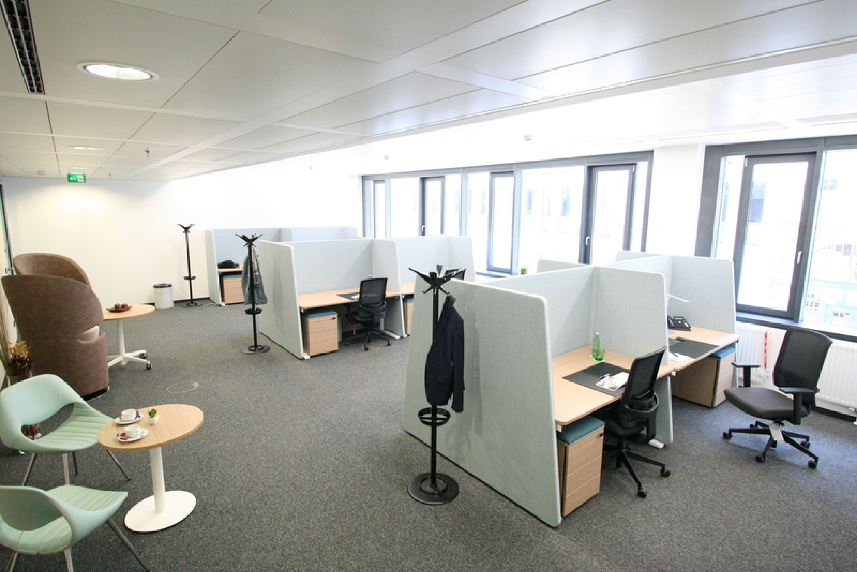 Geräumiges, modernes Büroinnere mit abgetrennten Arbeitsplätzen, ergonomischen Stühlen und einem kleinen Loungebereich mit Sesseln und Tischen.