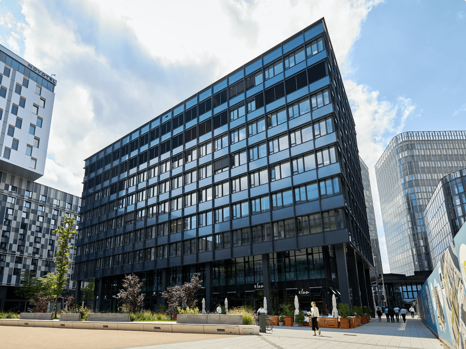 Exterior view of a modern glass and steel commercial building with people walking outside at QBC