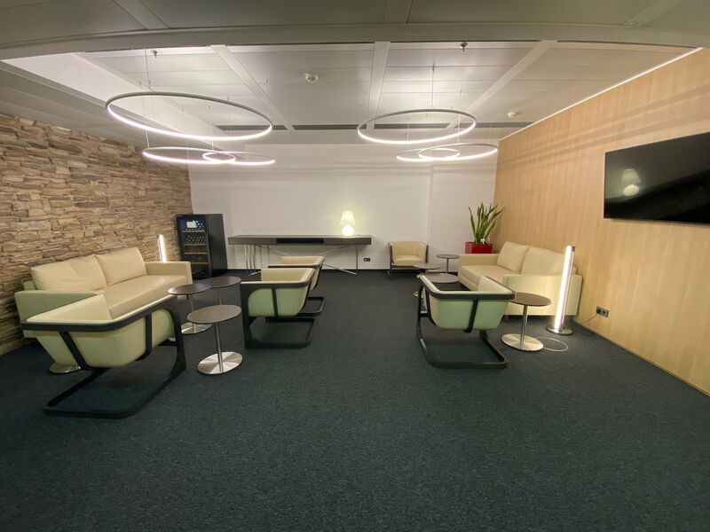 Geräumiger Loungebereich im Büro mit cremefarbenen Sofas, Sesseln, moderner Ringbeleuchtung, einer Stein-Akzentwand und holzverkleideten Wänden.