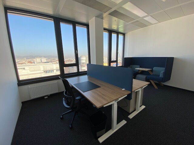 Heller, moderner Büroraum mit höhenverstellbaren Holzschreibtischen, ergonomischem Stuhl und großen Fenstern mit Blick auf die Stadt.
