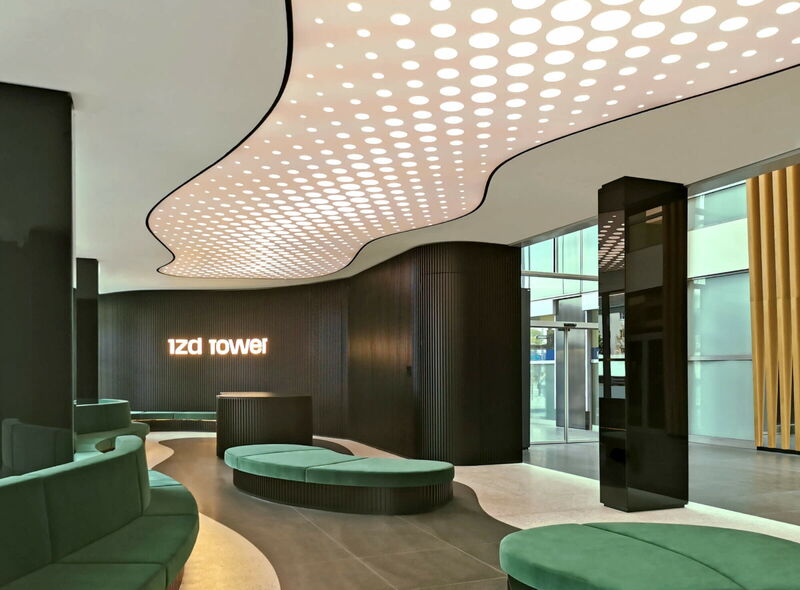 Modernes Interieur der IZD Tower Lobby mit geschwungener, beleuchteter Punktraster-Decke, dunklen Lamellenwänden und grünen Lounge-Möbeln.