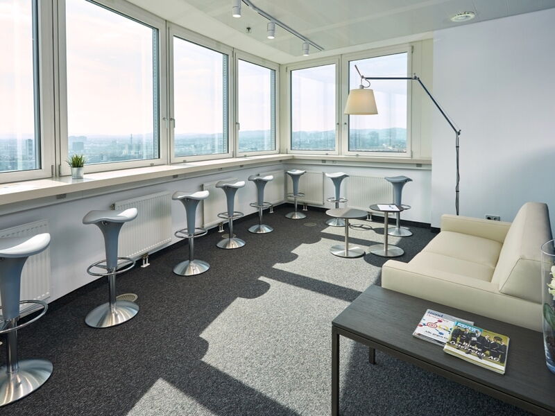 Moderner Pausenraum im Büro mit hohen Barhockern an großen Panoramafenstern und einem bequemen Sofa