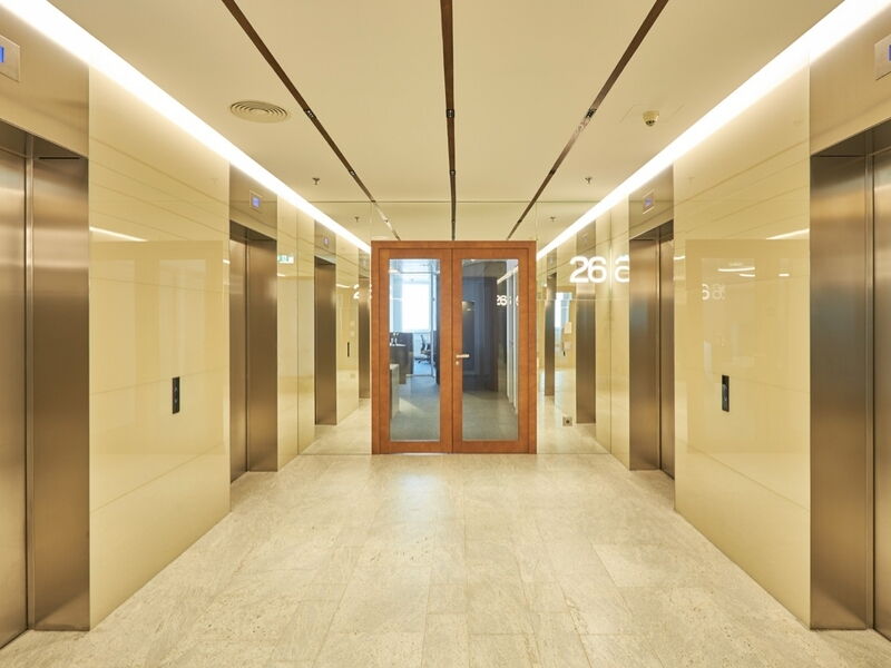 Moderne Büro-Flur mit metallischen Aufzügen, gefliesten Wänden und hölzernen Doppeltüren aus Glas am Ende.