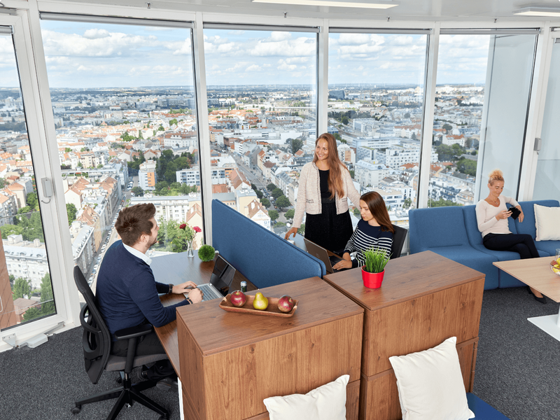 Mitarbeiter arbeiten in einem modernen, hellen Büro mit raumhohen Fenstern und Blick auf die Skyline