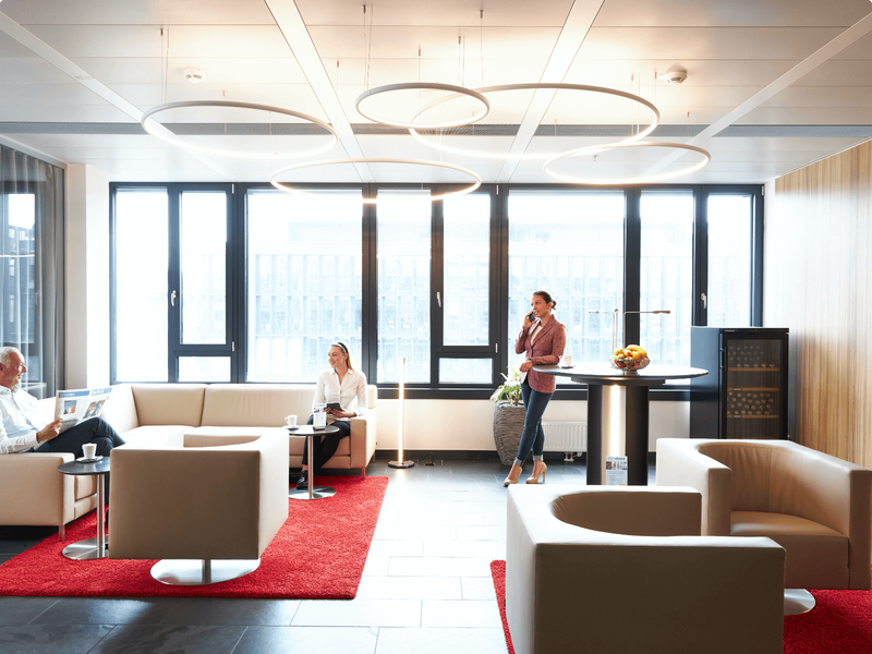 Geschäftsleute beim Networking in einer modernen, gut beleuchteten Büro-Lounge mit bequemen Sitzgelegenheiten und großen Fenstern.