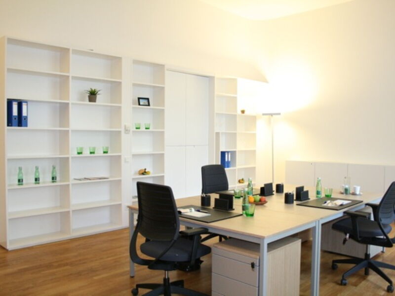 Moderne Büroausstattung mit großen weißen Regalen, Holztischen, schwarzen Bürostühlen und warmer Beleuchtung