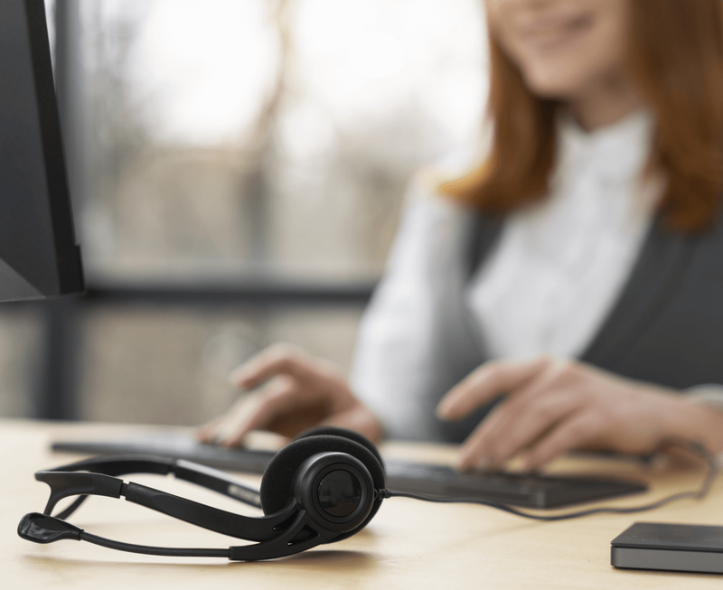Smiling female call center agent typing on keyboard with black headset in foreground