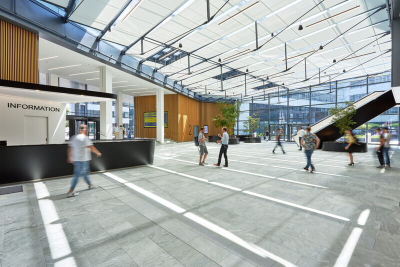 Helles und geräumiges modernes Bürogebäude-Atrium mit Glasdecke, Rezeption und gehenden Personen in der Halle.