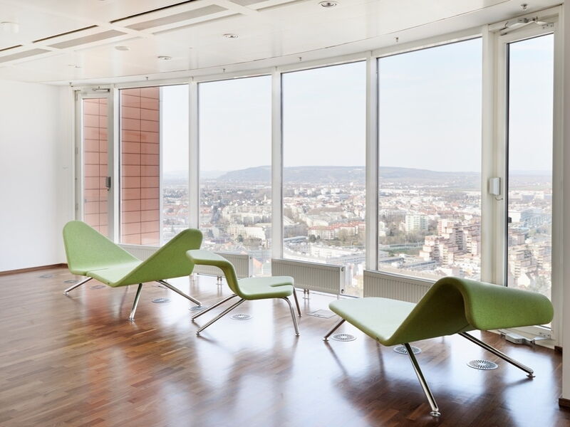 Heller Büroraum mit großen Fenstern, Parkettboden und modernen grünen Lounge-Möbeln mit Blick auf die Stadt