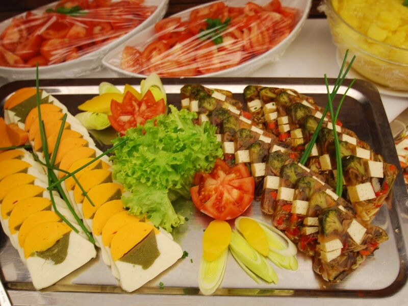 Eine Catering-Platte mit herzhaften Sülzestücken mit Gemüse und Tofu, gefüllten Eiern mit grüner Füllung, garniert mit Salat und Tomaten.