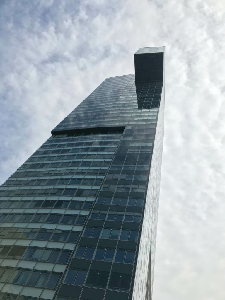 Low-angle view of a contemporary glass skyscraper with a distinctive top structure under a cloudy sky