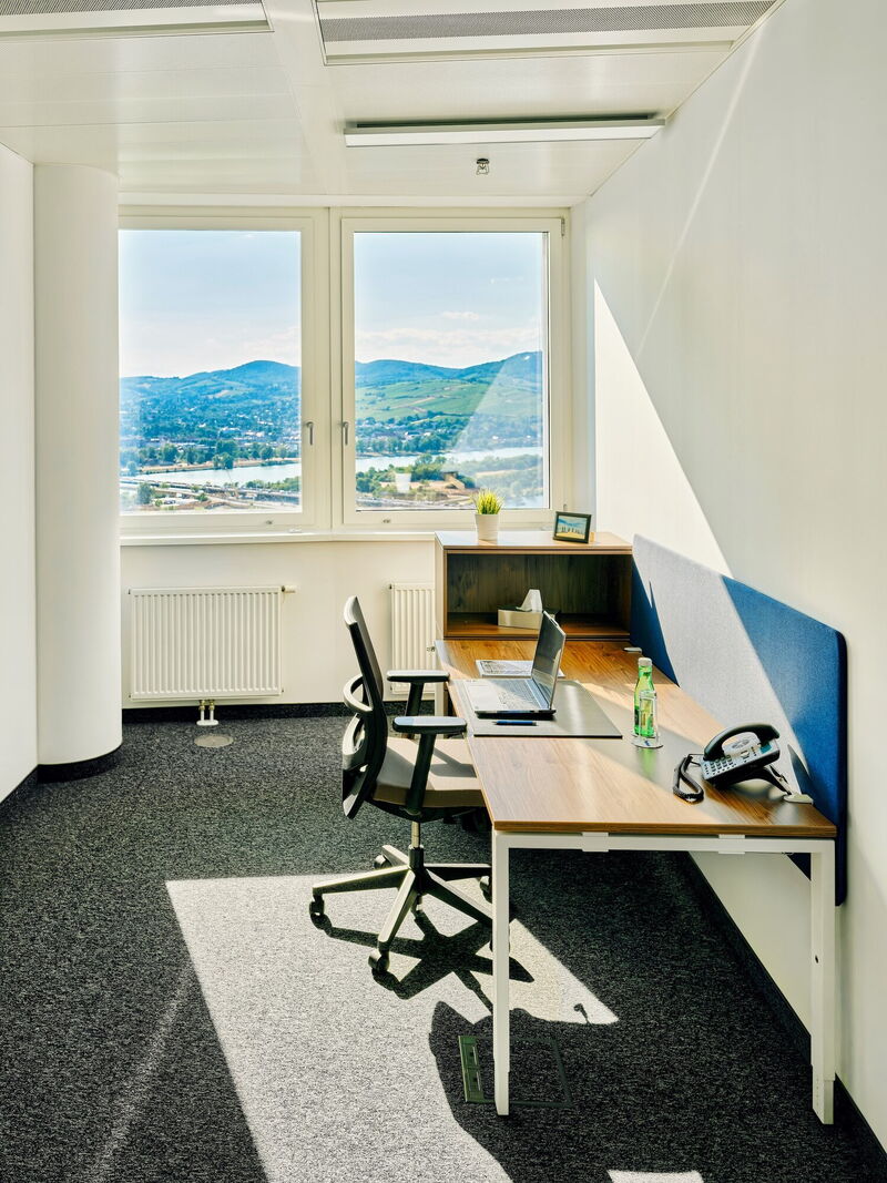 Heller, moderner Büroarbeitsplatz mit Laptop und Panoramablick auf Berge und Fluss durch große Fenster