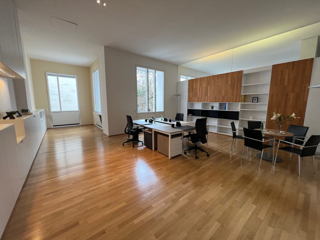 Geräumiges modernes Büro mit Holzboden, Schreibtischen, ergonomischen Stühlen und großen Fenstern für viel Tageslicht.