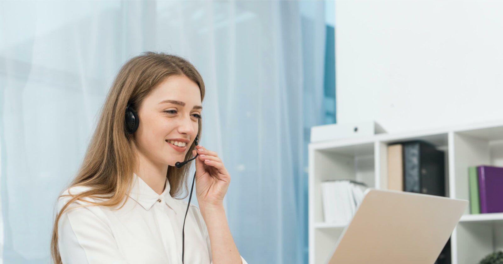 Lchelnde weibliche Kundendienstmitarbeiterin mit Headset whrend der Arbeit am Laptop