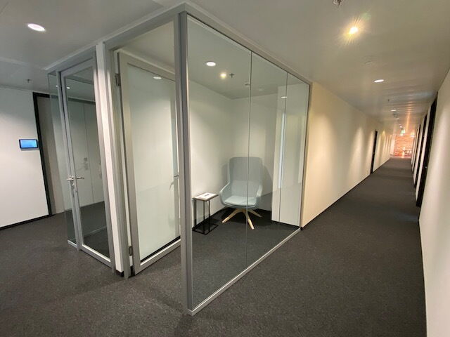 Modern office interior featuring glass meeting pods, a silent room with an armchair, and a long hallway with carpet flooring.