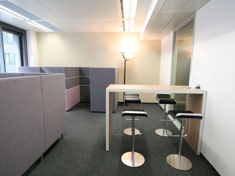 Moderne Büro-Lounge mit hellem Stehtisch, schwarzen Barhockern und Akustik-Trennwänden im Europlaza