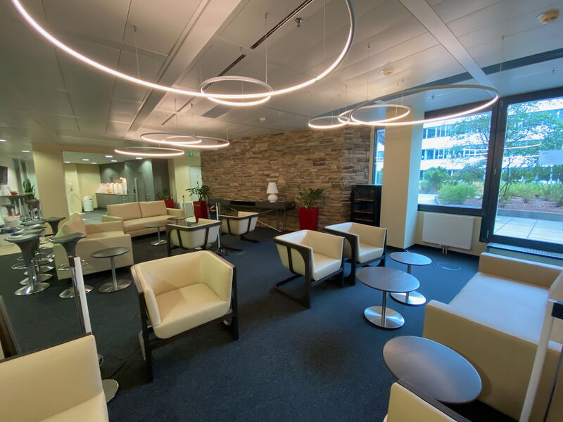 Geräumige Büro-Lounge mit cremefarbenen Sesseln, Sofas, kleinen runden Tischen, Steinwand und einzigartigen ringförmigen Pendelleuchten