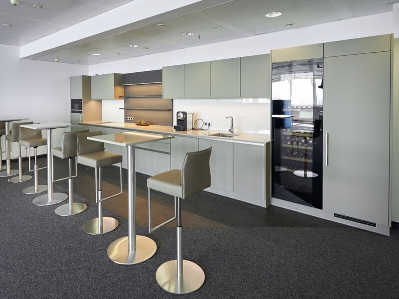 Schlichte, moderne Büroküche mit minimalistischen grauen Fronten, hohen Stehtischen mit Leder-Barhockern und einem eingebauten Weinkühlschrank.