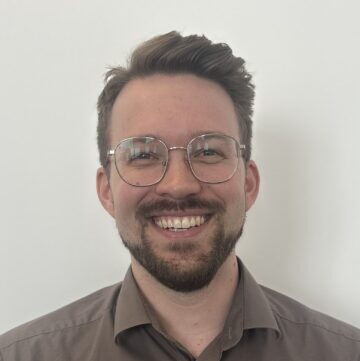 Portrait of Simon smiling wearing glasses and a brown shirt for career and team introduction