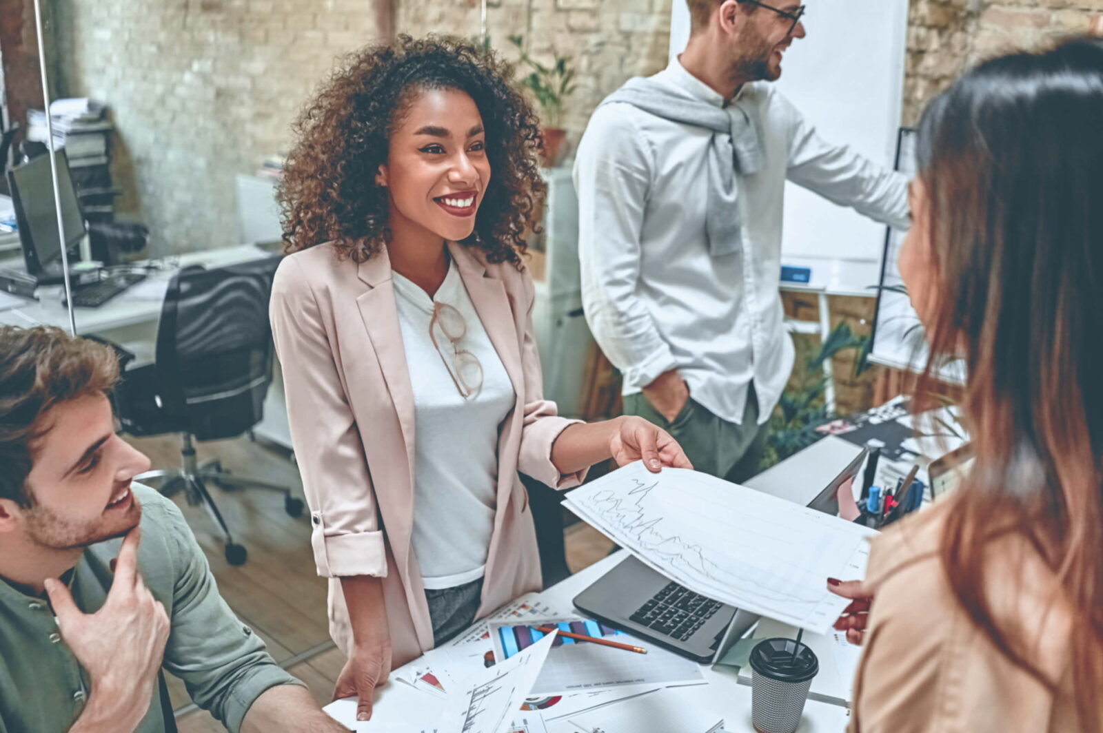 A smiling young woman handing business charts to a colleague during a team meeting in a modern office